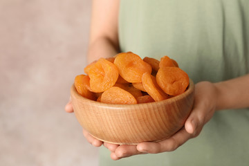 Woman holding bowl with dried apricots on color background, space for text. Healthy fruit