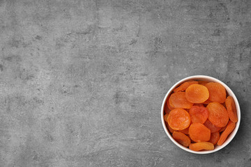 Bowl of dried apricots on grey background, top view with space for text. Healthy fruit