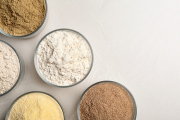 Bowls with different types of flour on light background, top view. Space for text