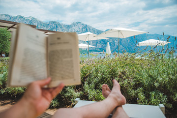 summer vacation. man laying on sun lounger reading book with beautiful view