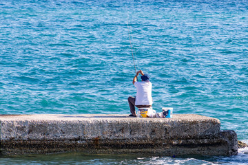 Fototapeta na wymiar A man is fishing on one of the docks in the port of Zakynthos, Greece
