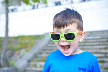 Scared surprised astonished mixed Caucasian male child with sunglasses, poses against brick white wall background.