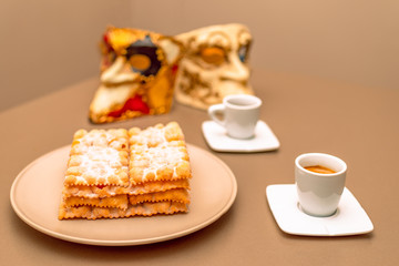 Typical Italian carnival fritters (Chiacchiere di Carnevale) dusted with powdered. Composition with two cups of coffee and in the background are Venetian carnival masks. 