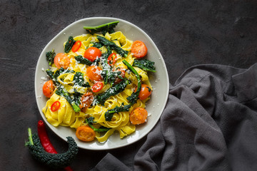 Tagliatelle pasta with kale, tomatoes, pepper and parmesan cheese. Dark background.