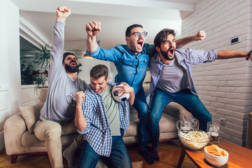 Men watching sport on tv together at home screaming cheerful.