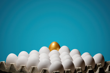 Concept of individuality, exclusivity, better choice. One golden egg among white eggs on blue background.