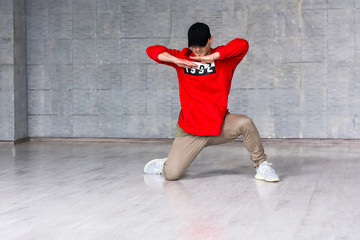 Young dancer posing on grey floor. Stylish hip-hop dancer making movement with hands on grey background.