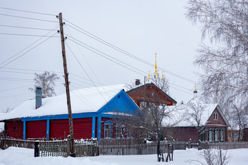 Snow-covered rural, wooden and brick houses. Orthodox church in overcast weather, a lot of snow.