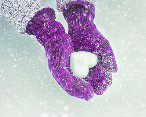Female hands in knitted mittens with heart of snow in winter day. Love concept. Valentine day background.