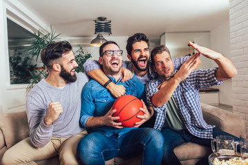 Happy friends or basketball fans watching basketball game on tv and celebrating victory at...