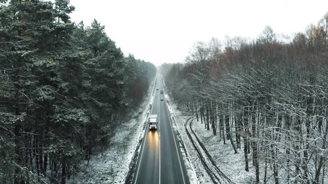Drone view of the beautiful winter landscape in snowy weather. Cars driving along a straight road in the forest covered with snow.