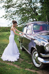 The happy, beautiful bride standing near the old car and opening the door