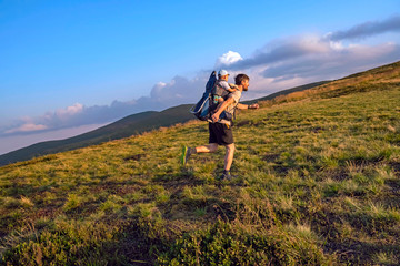 Father with baby in the backpack carrier runs up the mountain. Travel adventure and hiking activity with child, active and healthy lifestyle.