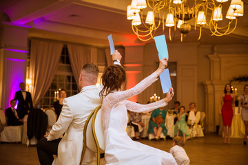 Back view of the happy newlyweds who are playing the game in the restaurant and sitting on the chairs