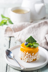 Piece of mango mousse cake on plate over white wooden table.
