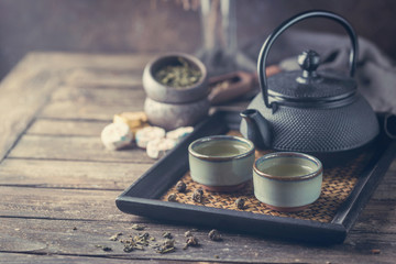 Still-life of japanese healthy green tea in a small cups and teapot over dark background