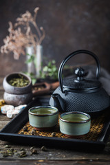 Still-life of japanese healthy green tea in a small cups and teapot over dark background