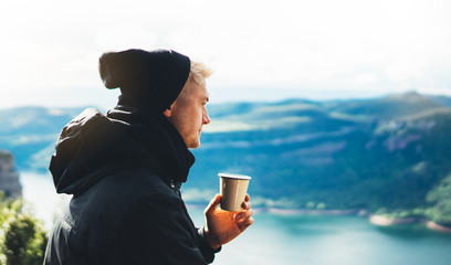 hipster tourist hold in hands mug of hot drink, lonely guy enjoy sun flare mountain in auto,...