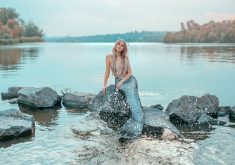 fair-haired mermaid in love dreams of handsome prince, new story Ariel, image of fairy-tale siren with long fish tail, chic crown of shells, plays, sprinkles clear water, ecology of environment