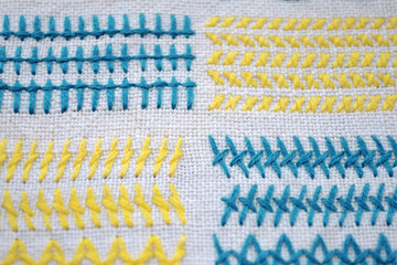 Different examples of yellow and blue square patterns of embroidery on white fabric