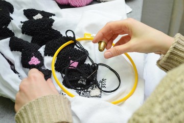 The woman embroiders by hand embroidery on white fabric with black and pink wool threads in hoop, left view