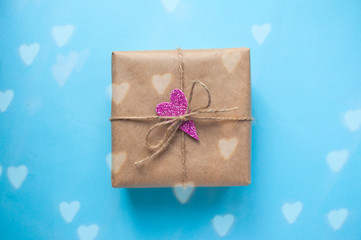 Gift box wrapped in brown colored craft paper with pink glittering heart and tied with rope on blue background.