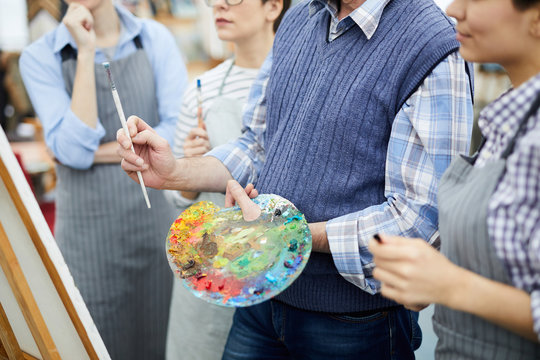 Mid section portrait of unrecognizable artist holding palette while working with group of students in art class, copy space