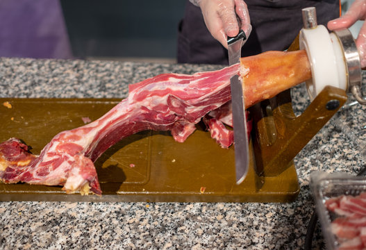 The process of cutting the delicious Spanish ham from pork leg, attached to a wooden board.
