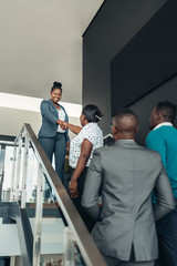 Smiling confident black businesswoman greeting and shaking hands with all african woman on stairs