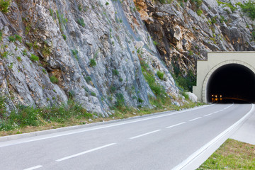 Road and tunnel in the mountain. Cars driving out of it with glowing headlights