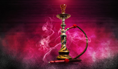 Smoking hookah on the background of an empty wooden wall and concrete floor. Spotlight, red neon light, smoke