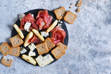 Slate plate with delicacies: jamon, blue cheese, brie. View from above.