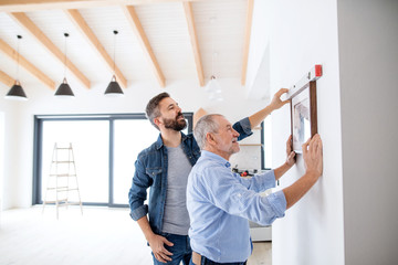 A senior man helping his son hanging up pictures on wall, a new home concept.