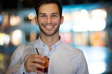 Young man holding a drink at a night club outdoor