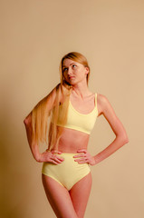 Obraz premium thin and attractive blond woman wearing a lemon-colored underwear posing for pictures in studio on beige background