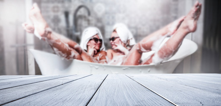 Two beautiful women in a bathtub with a lot of foam and a wooden table for an advertising product