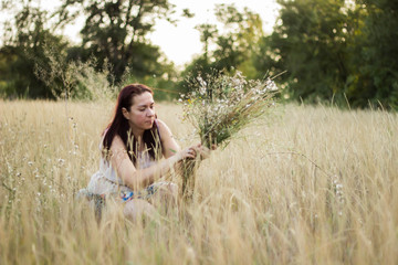 Cute girl in a long light dress is having fun, dancing and gathering wild flowers and spikelets