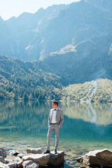 Handsome groom in wedding suit standing on the stony lake shore in the mountains. Morskie Oko