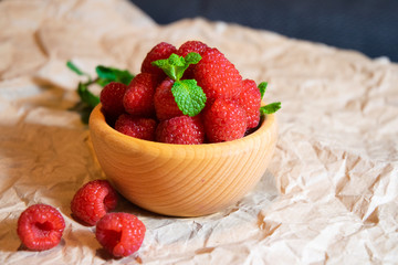 Wooden bowl with juicy delicious red raspberries decorated with fresh mint