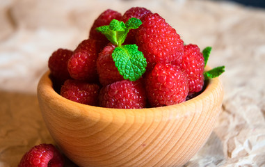 Wooden bowl with juicy delicious red raspberries decorated with fresh mint