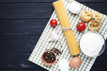 Different pasta with garlic, tomatoes, eggs and flour on wooden table