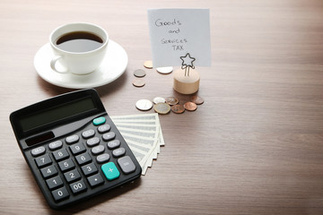 Inscription Goods and Services Tax with calculator, banknotes, coins and cup of coffee