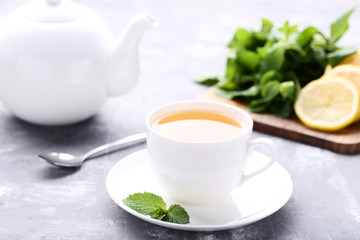 Cup of tea with mint leafs and teapot on wooden table