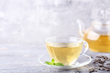 Cup of tea with mint leafs and teapot on grey wooden table