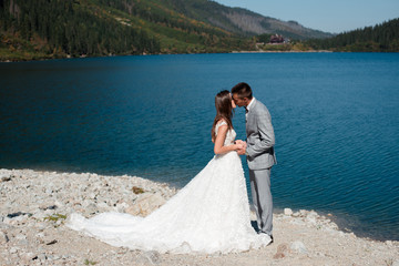 Groom and bride kissing while standing on the lake shore in Tatra mountains. Morskie Oko, Poland