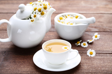 Cup of tea with chamomile flowers on brown wooden table