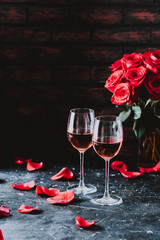 Two wine glasses of rose wine on brick background, bouquet of red roses for romantic evening for Valentines day surprise, marriage proposal passion and love celebration, copy space 