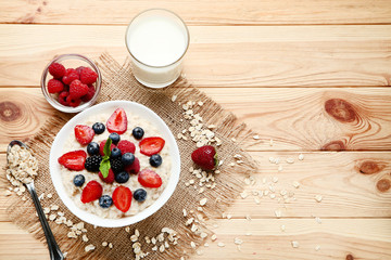 Oatmeal with berries in bowl and glass of milk on wooden table