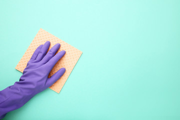 Hand in glove with sponge on mint background