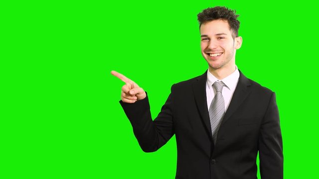 Young businessman pointing his finger to the left, product placement concept, isolated on green screen chroma key background